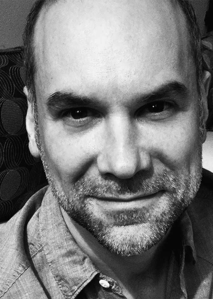 Close-up portrait of a man with a beard, smiling. Greg Stuhr