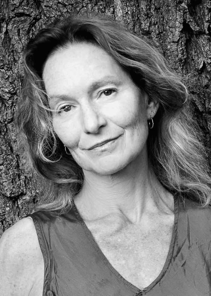 Paola Styron, smiling woman with long hair, leaning against a tree