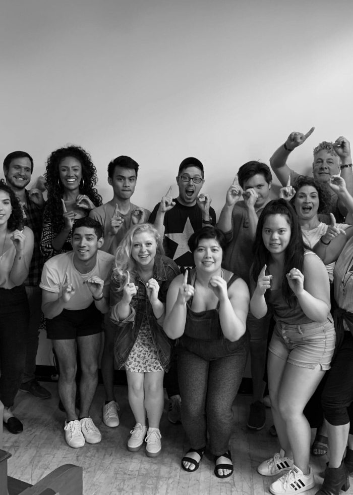 Group of young adults posing, making hand gestures. Could be a theater group.
