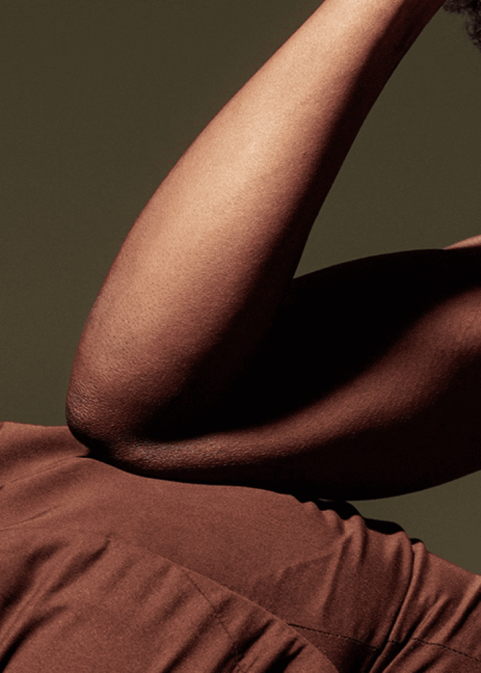 Close-up of two people embracing, highlighting a strong arm and shoulder against a dark background.