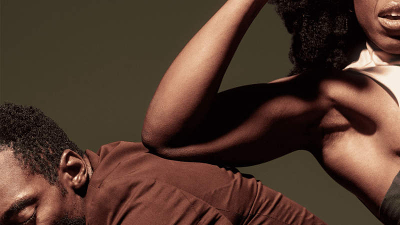 Close-up of two people embracing, highlighting a strong arm and shoulder against a dark background.