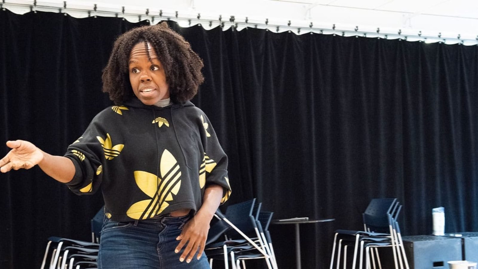 Woman in Adidas hoodie gestures during rehearsal.