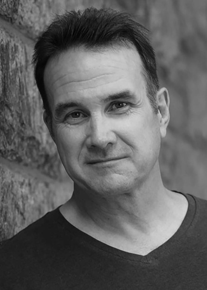 Ted Koch looking at the camera, leaning against a stone wall.