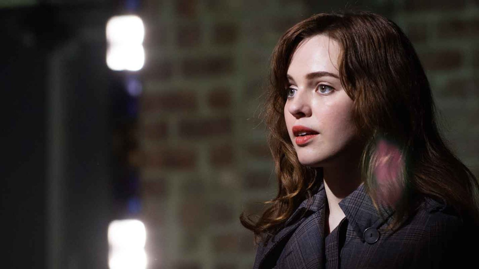 A pensive young woman with long brown hair, looking off to the side.