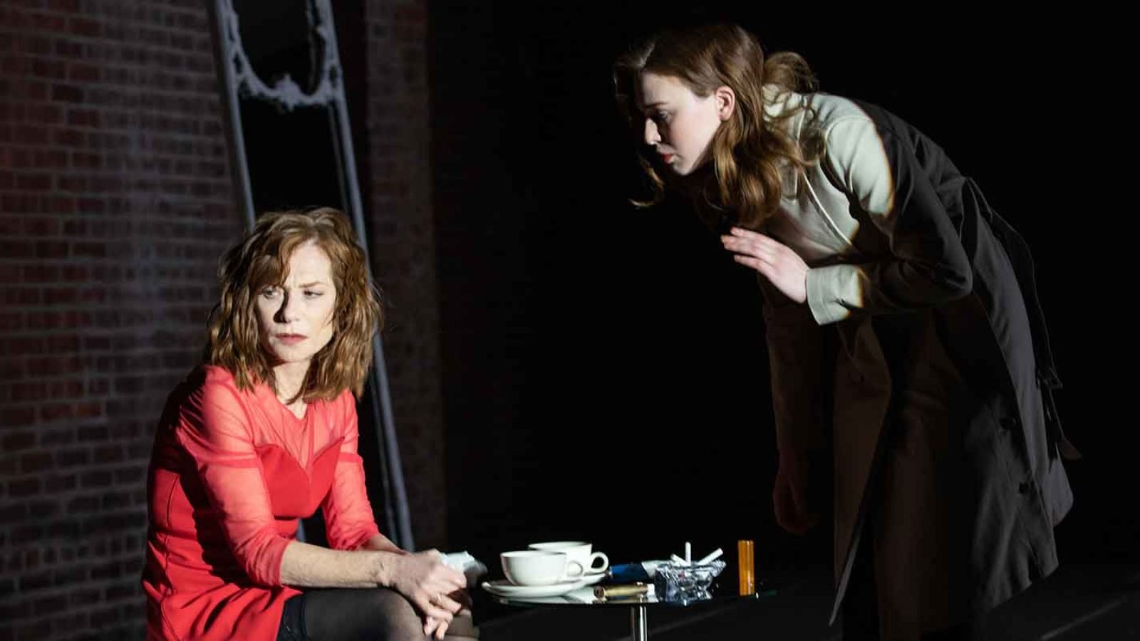 A mother and daughter share a tense moment, coffee cups on a table between them.