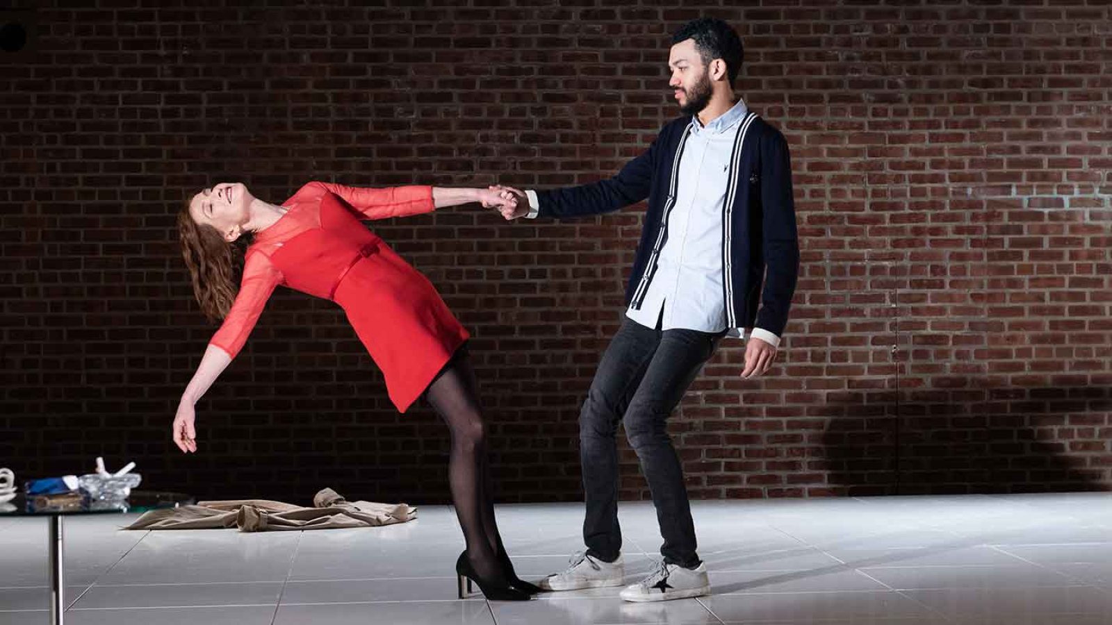 A woman in a red dress is playfully held by a man against a brick wall.