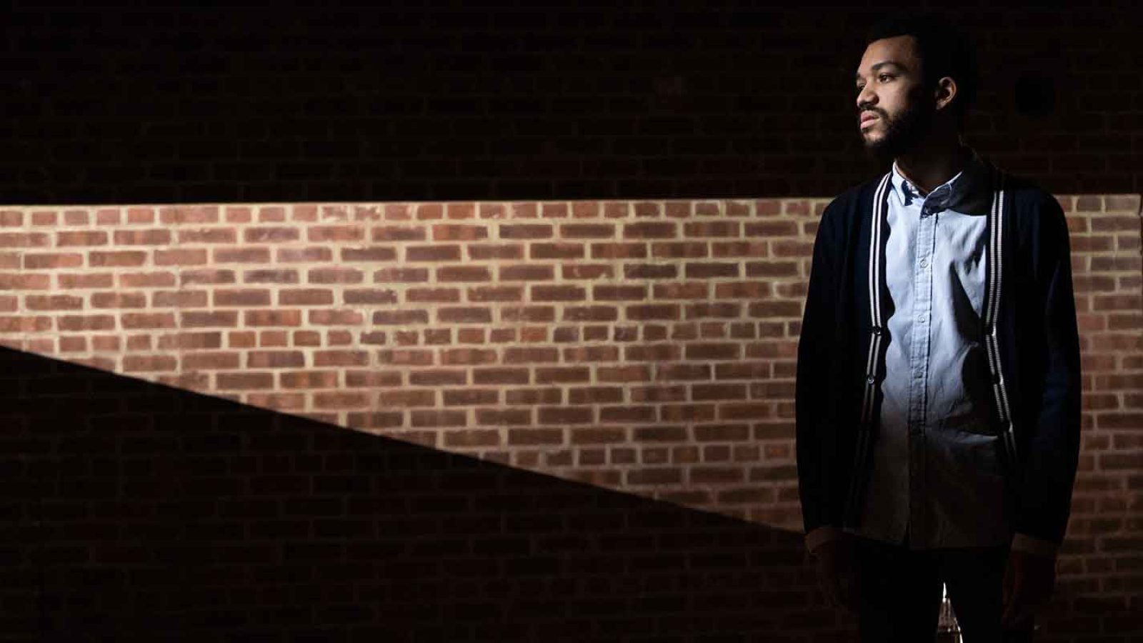 Thoughtful young man standing against a brick wall
