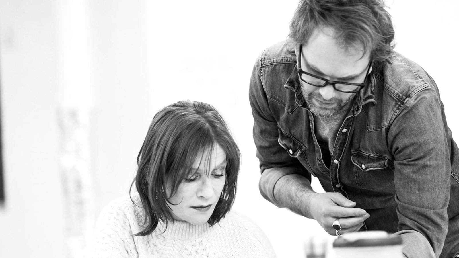 A man and woman collaborate closely, leaning over papers; the mother's pensive expression is visible.