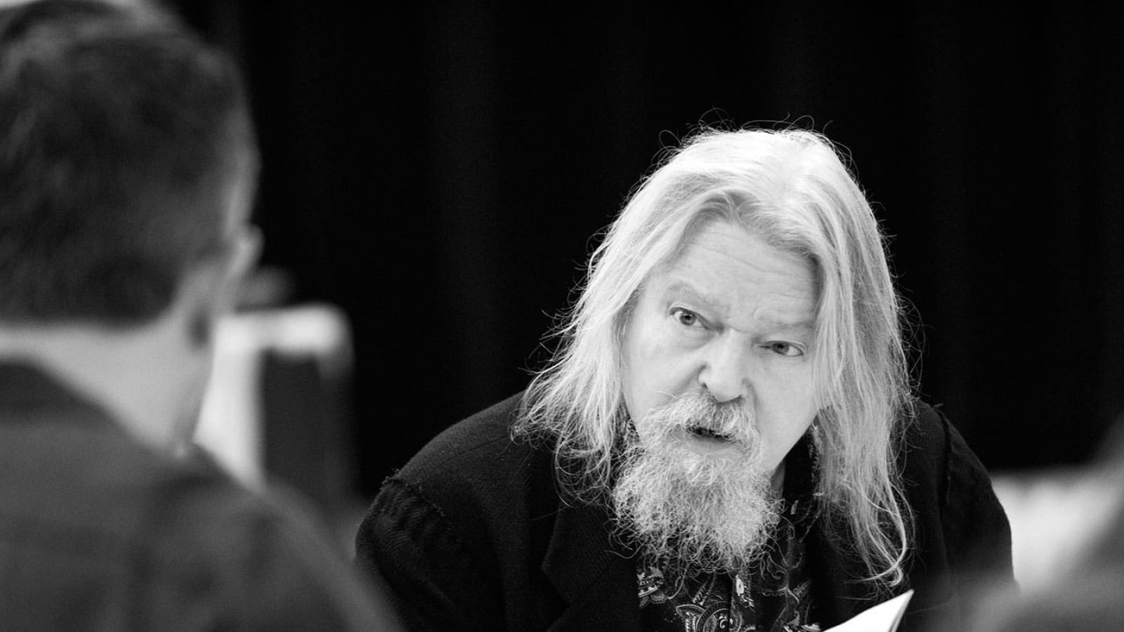 Close-up of a man with long gray hair and beard, appearing thoughtful.