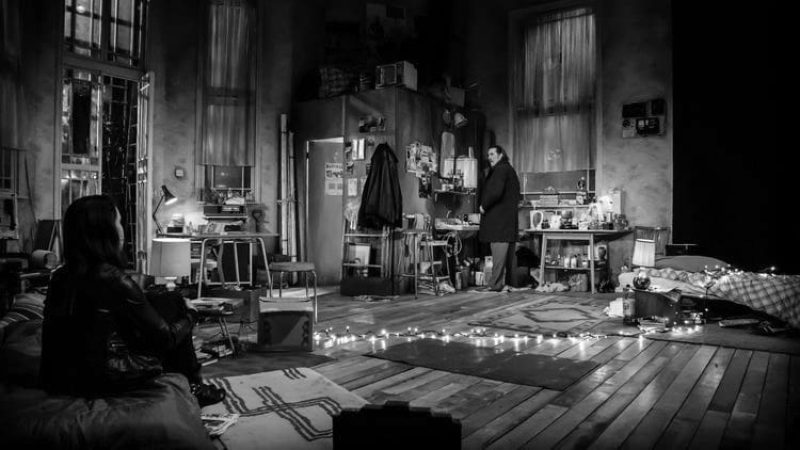 Black and white photo of a cluttered room from the play 'The Night Alive', featuring two people.