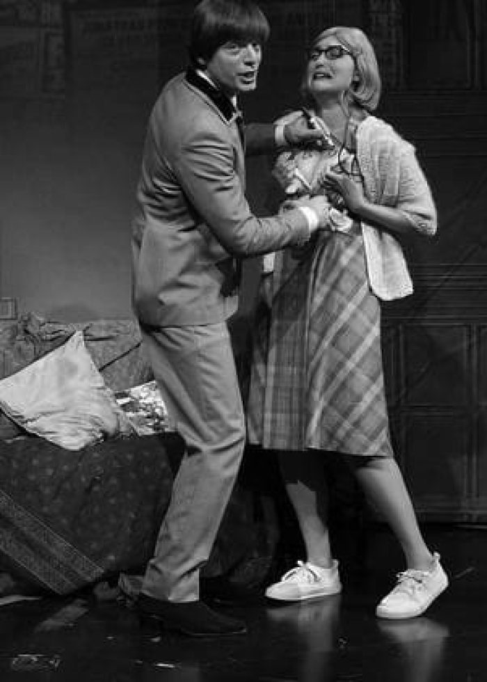 Actors in a scene from "These Paper Bullets!" A man in a suit gestures towards a woman.
