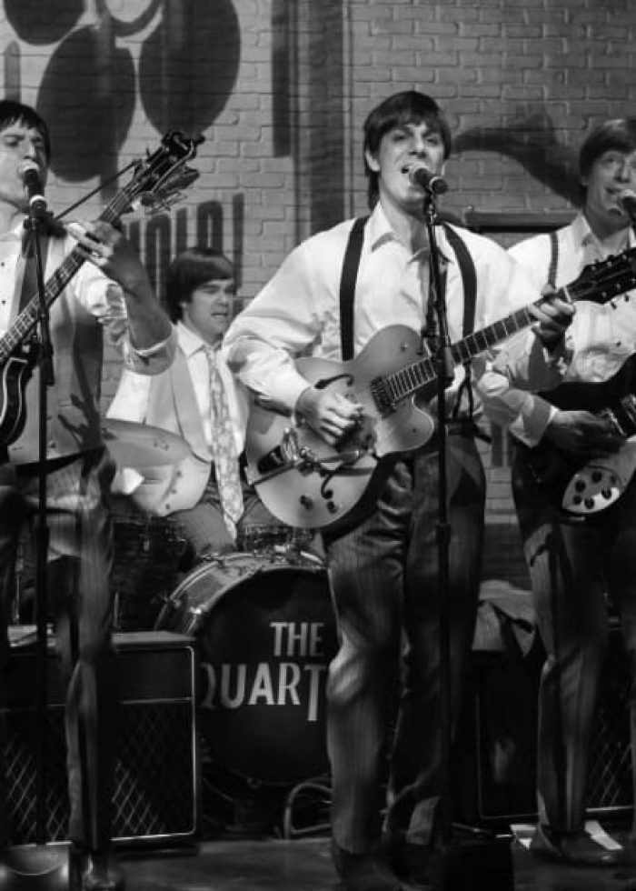 The Quartets, a Beatles tribute band, playing guitars and singing live on stage.