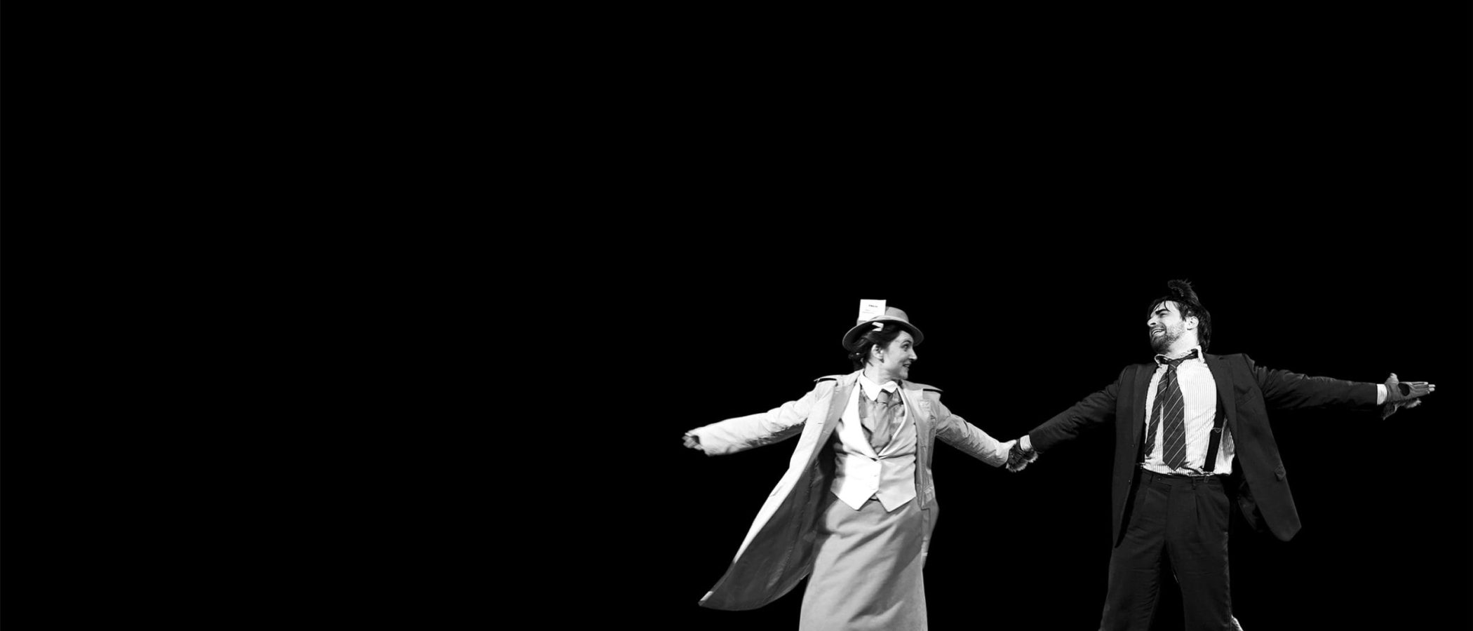 A man and woman in 1930s attire playfully dance, holding hands.