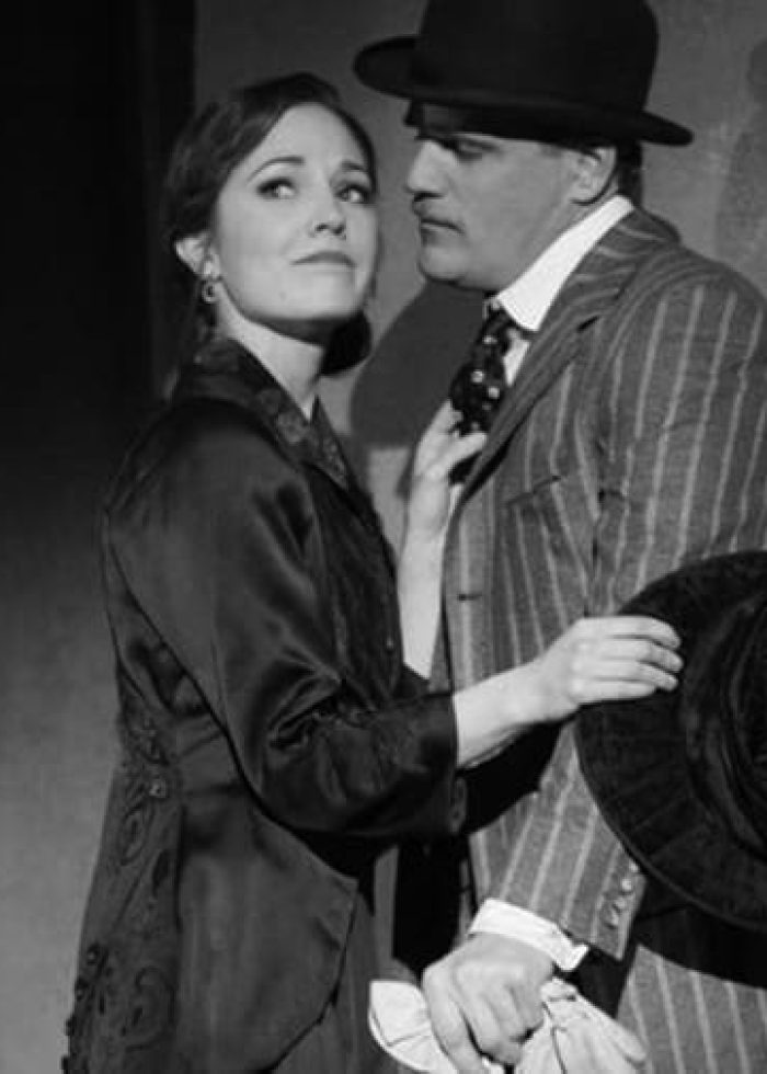 Scene from Threepenny Opera: A woman touches a man's tie in a theatrical performance.