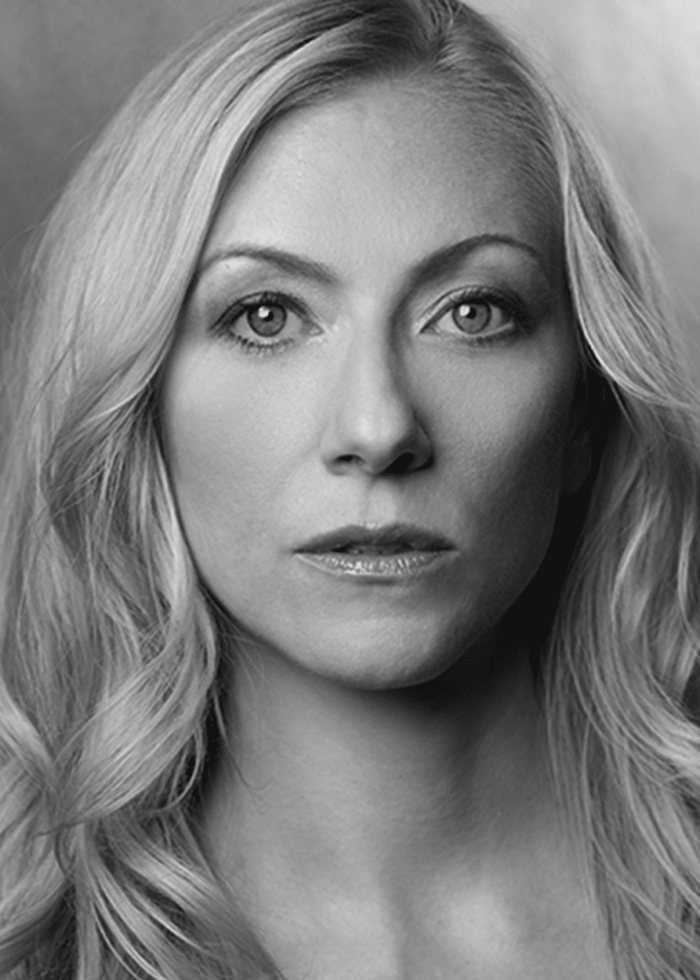Woman with long blonde hair looking directly at the camera in a black and white headshot.