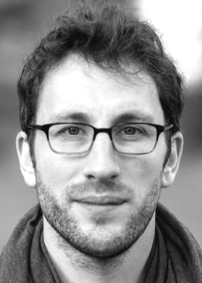 Tom Costello wearing glasses, looking at the camera