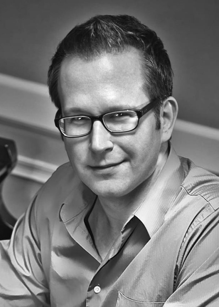 Tommy Newman, wearing glasses, smiles in a black and white photo.