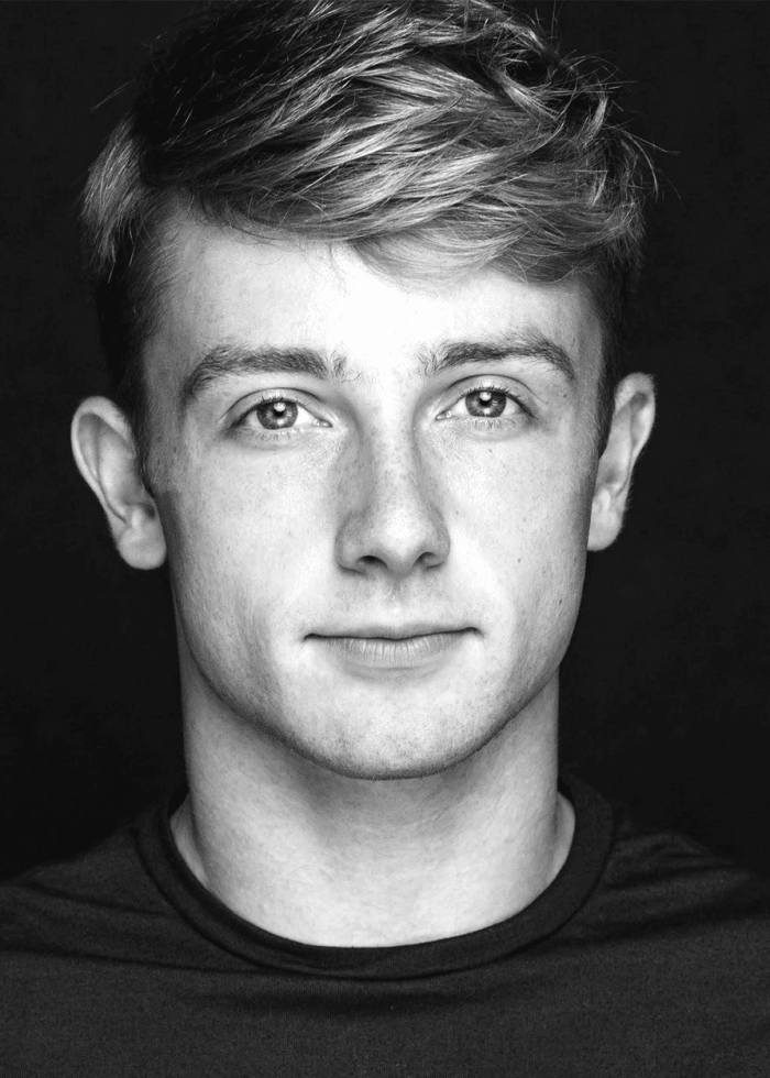 Close-up portrait of a young man with blonde hair, looking directly at the camera.