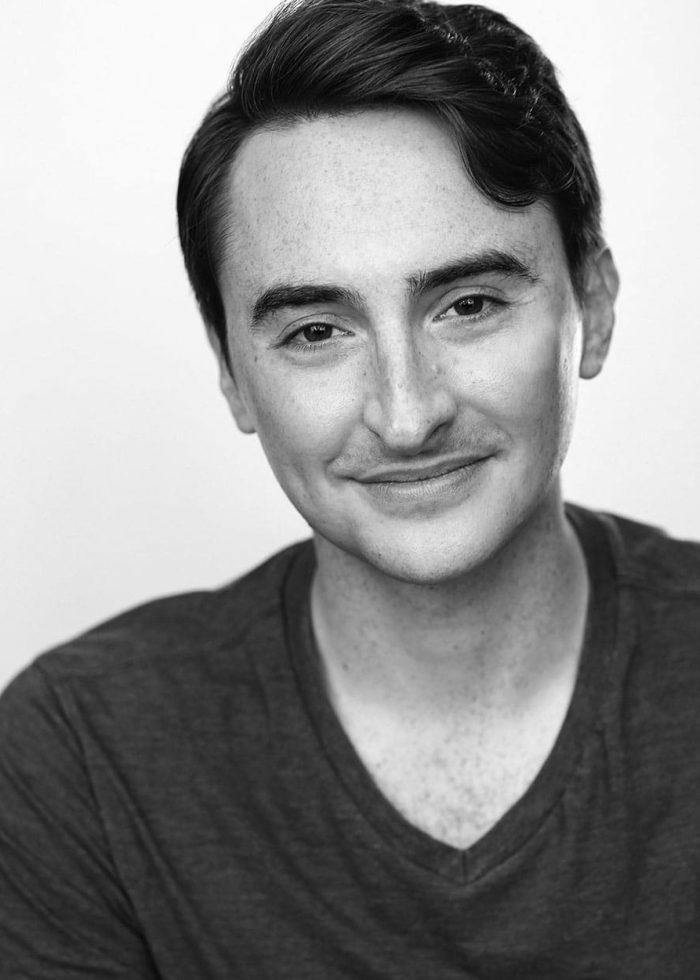 Man smiling, wearing a dark v-neck shirt, with freckles