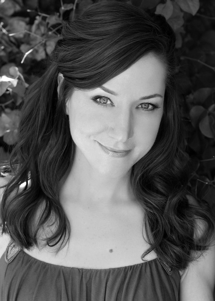 Seana Kofoed smiles with wavy brown hair, looking directly at the camera