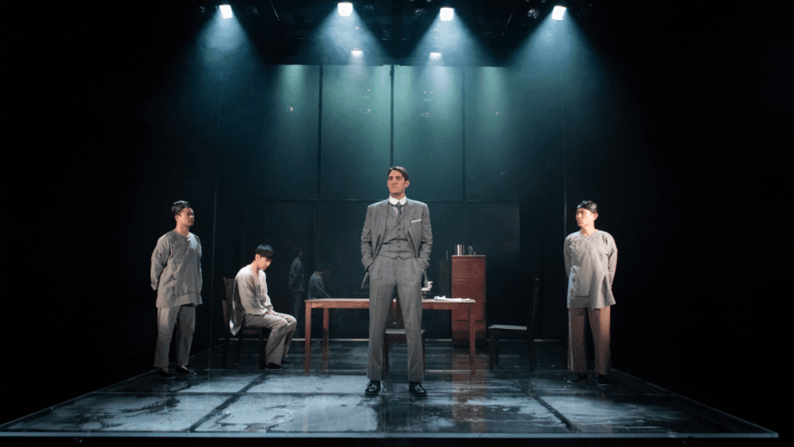 A man in a suit stands center stage, flanked by three men in loose-fitting gray clothing. The Far Country.