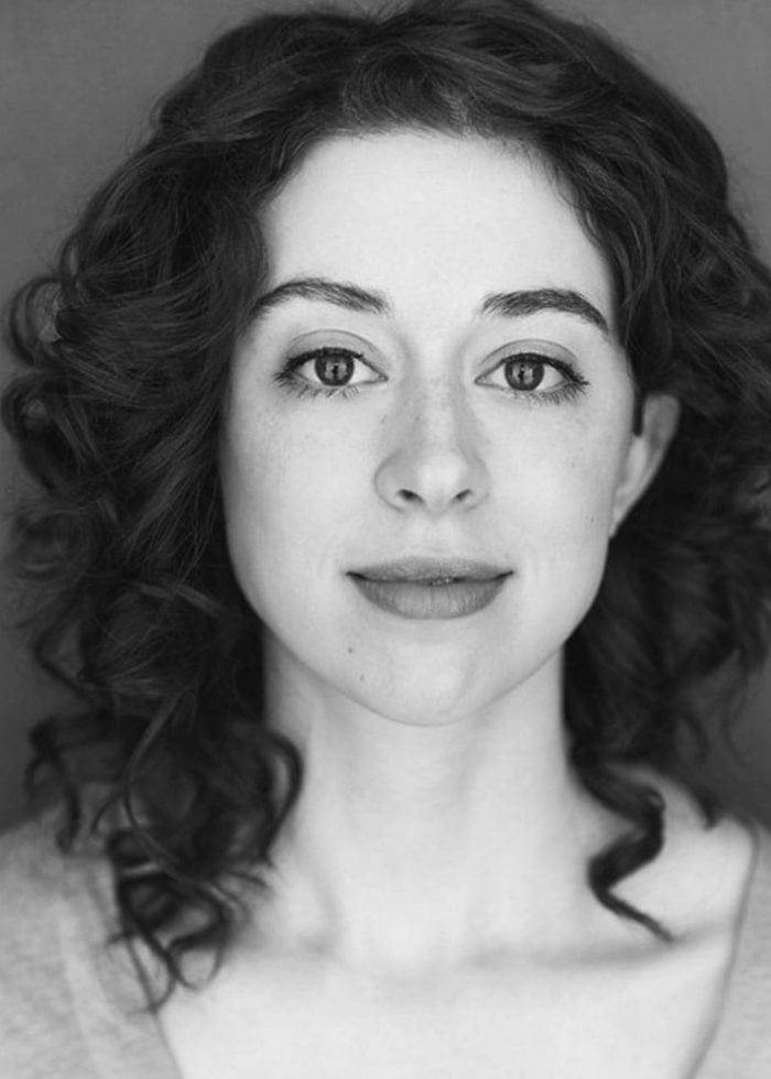 Adina Verson, a woman with curly hair, looking directly at the camera.