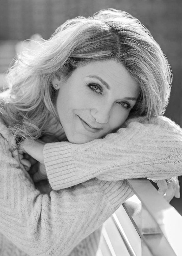 Victoria Clark smiles, leaning on a railing, in a sweater.