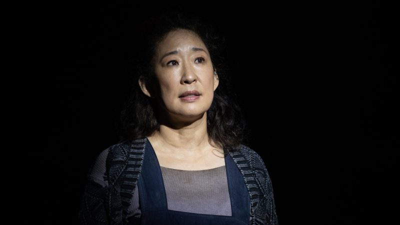 New York Music Photographer Sandra Oh in a dimly lit scene, looking up with a contemplative expression.