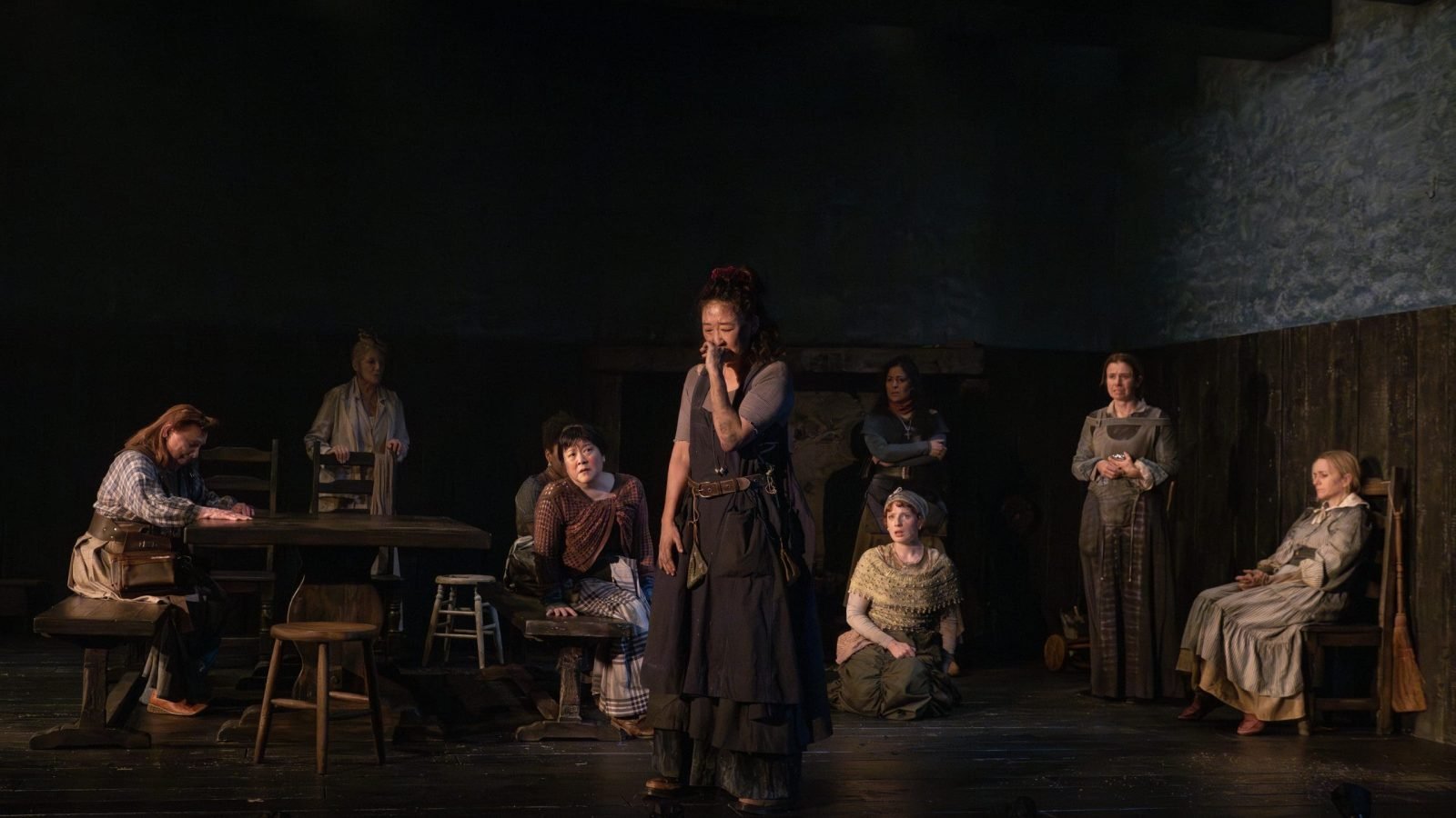 A group of women in period costumes, one weeping center stage, during a performance of *The Welkin*.