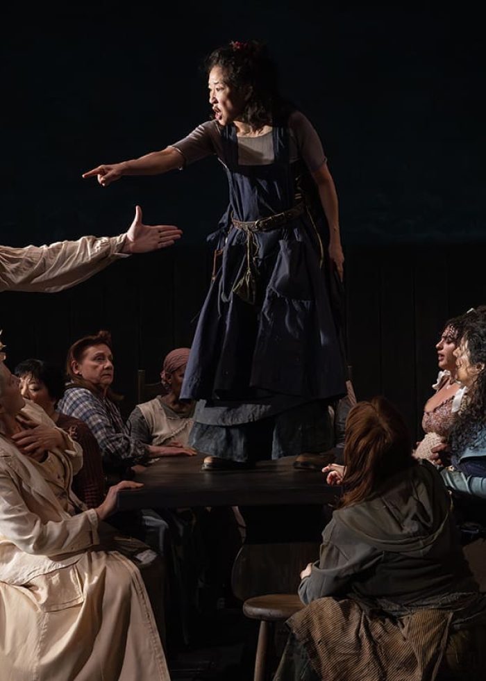 Scene from "The Welkin" play: Woman on table points, surrounded by actors. Critics' Pick logo visible.
