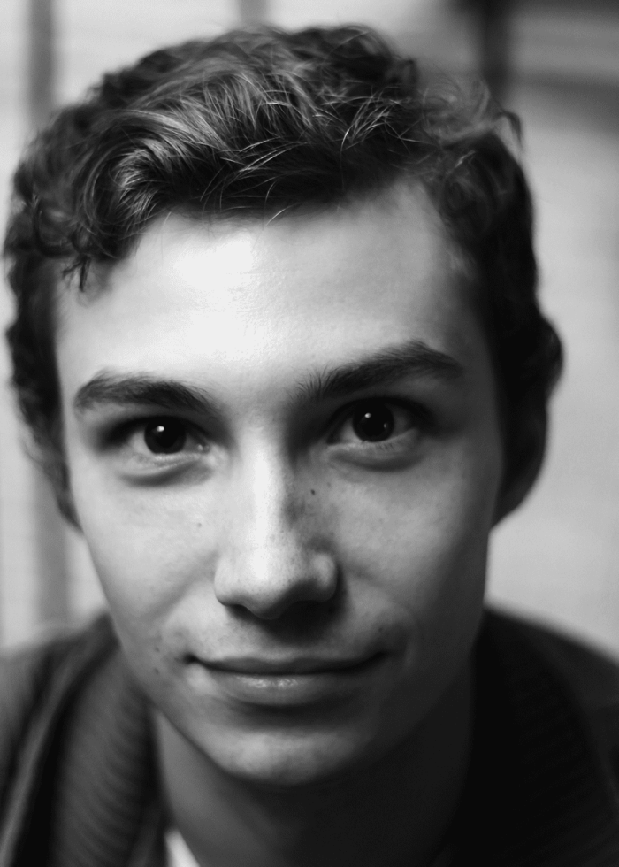 Wesley-Zurick-Headshot Close-up portrait of a young man with curly hair, smiling gently.