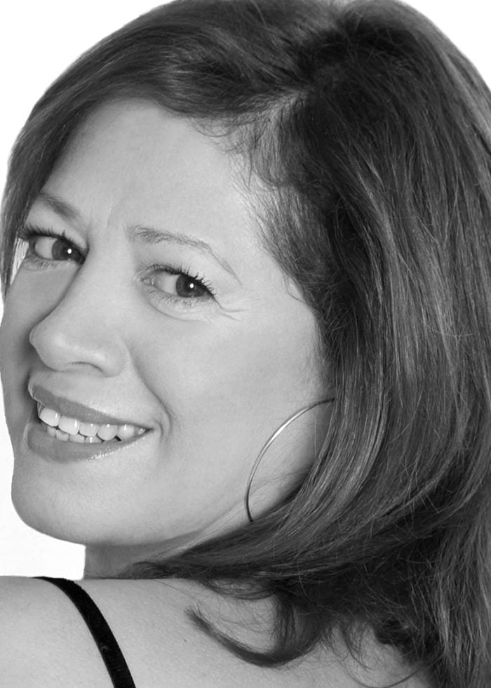 Smiling woman with brown hair wearing hoop earrings, looking over her shoulder.