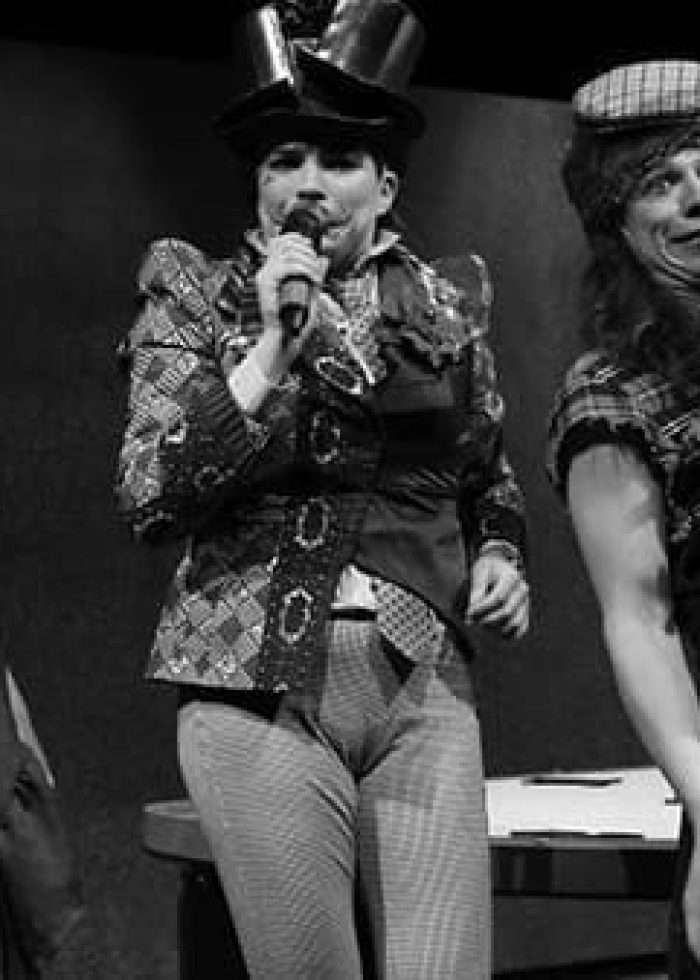 Three performers in costume singing into microphones on stage for Wonderland: Alice’s Rock & Roll Adventure.