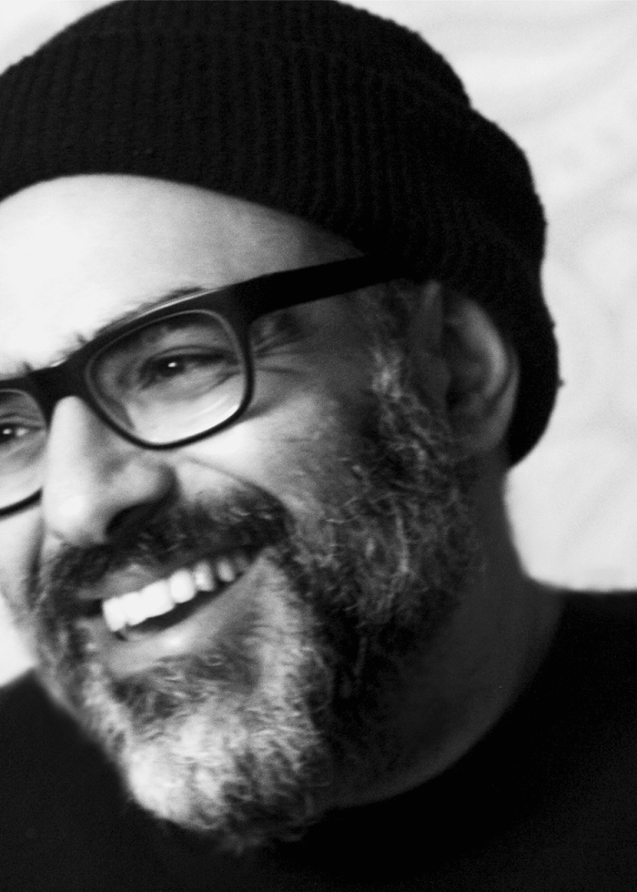 David Yazbek smiling, wearing glasses and a black beanie