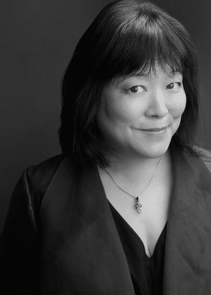 Ann Harada, smiling, wearing a dark jacket and necklace.