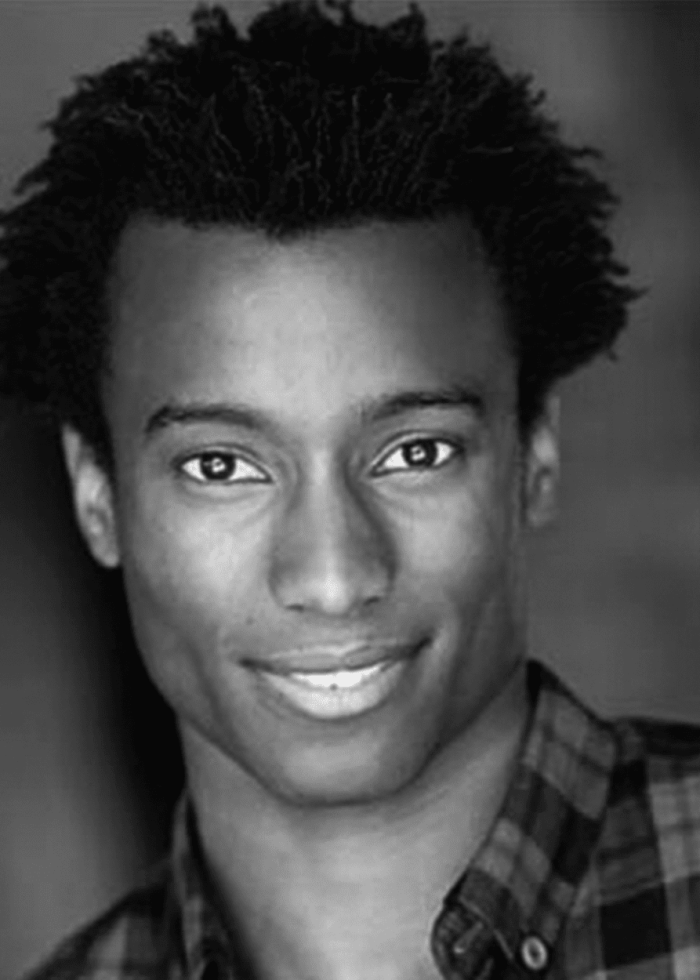 Black and white headshot of Sheldon Best smiling in a plaid shirt.