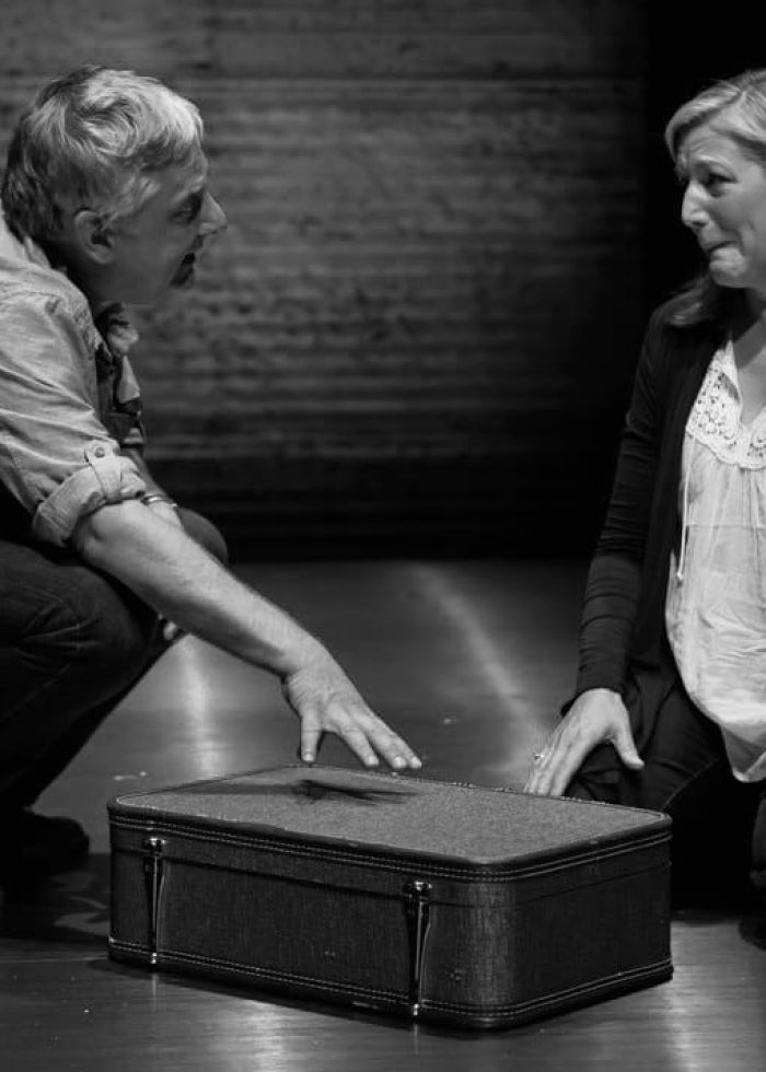 Actors in a scene from "Bluebird," kneeling near a suitcase, appearing emotional.