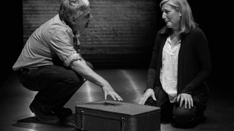 Actors in a scene from "Bluebird," kneeling near a suitcase, appearing emotional.