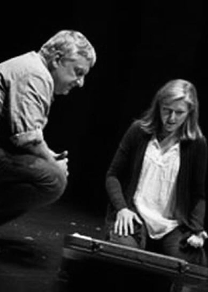 Actors on stage in a scene from "Bluebird", looking down at a prop.
