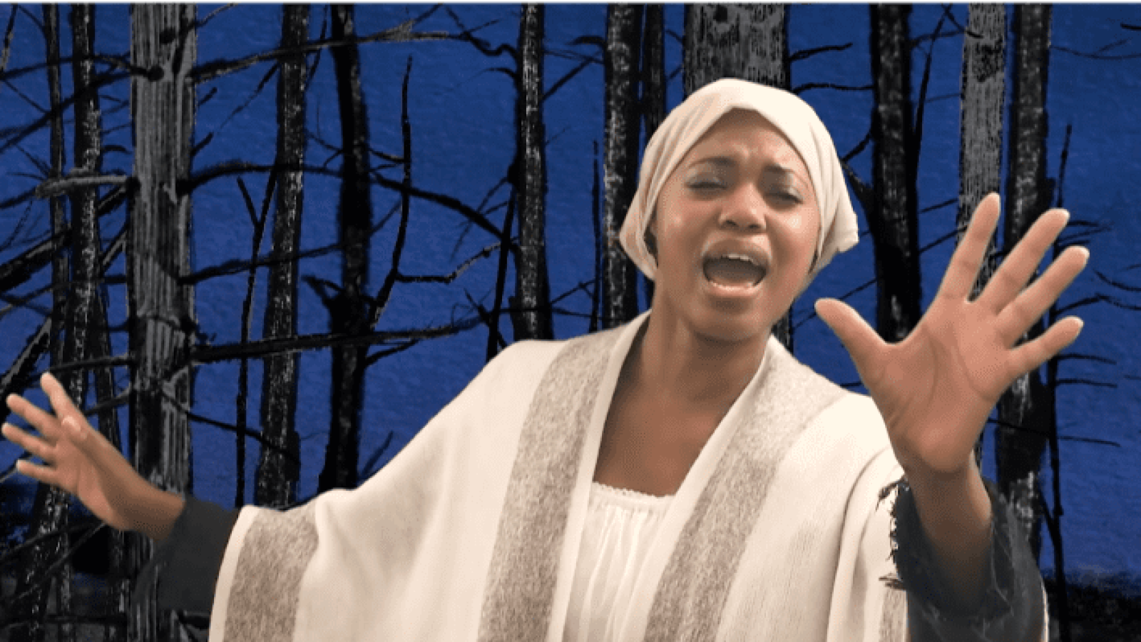 A woman in a white robe sings passionately, hands outstretched, against a dark forest backdrop. She Persisted, The Musical.