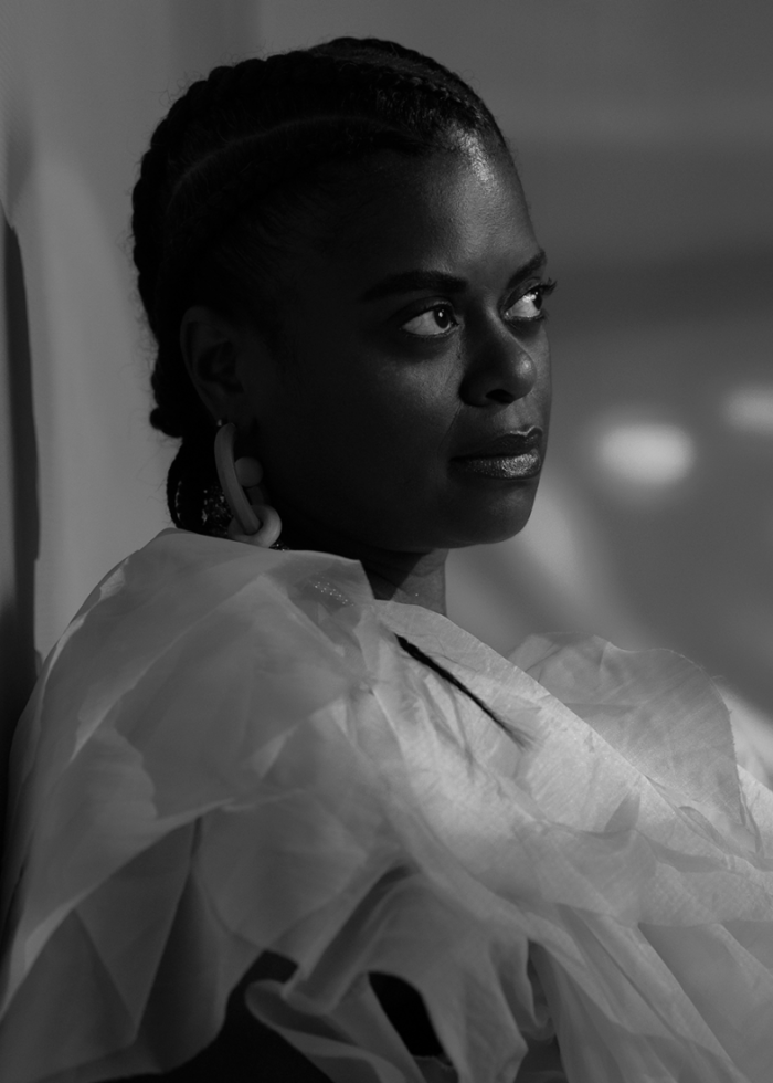 Black and white portrait of DJ Monday Blue, looking off to the side with braids.