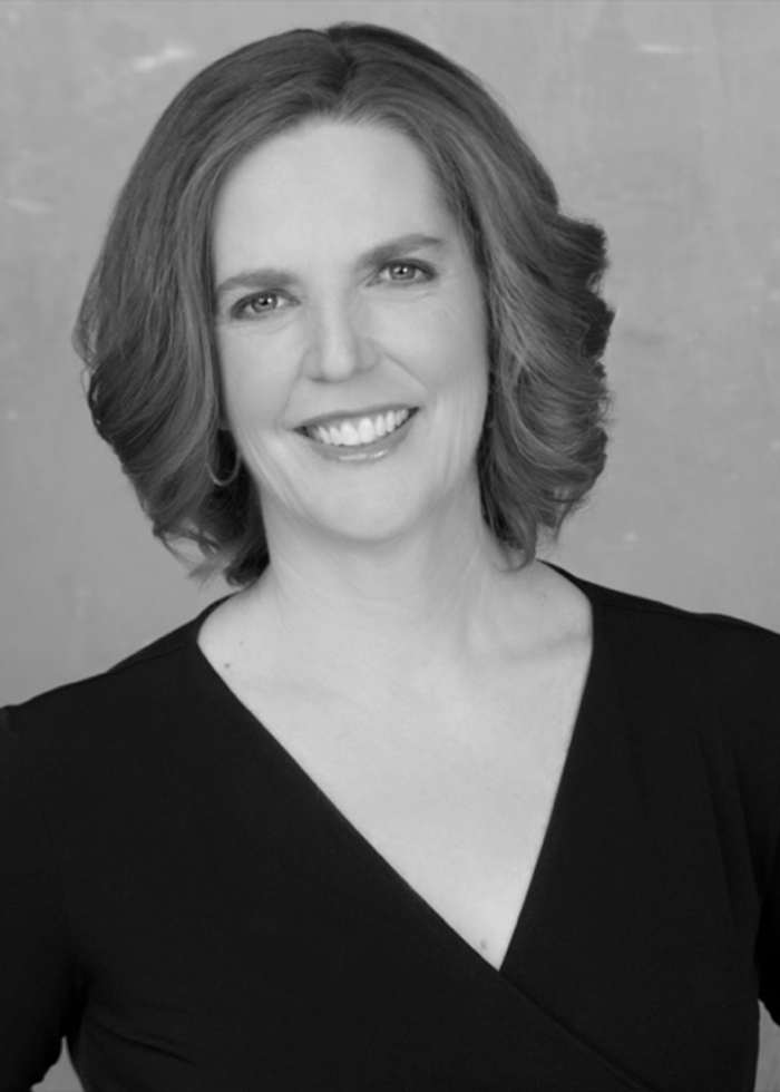 Deborah Wicks La Puma, smiling headshot in black dress with curled hair.