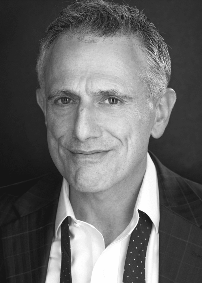 David Greenspan portrait: Man in suit smiling at camera.