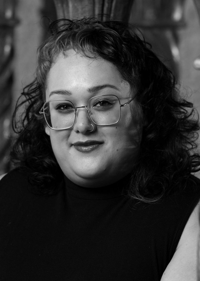 Woman with glasses and nose ring, smiling in black and white portrait.