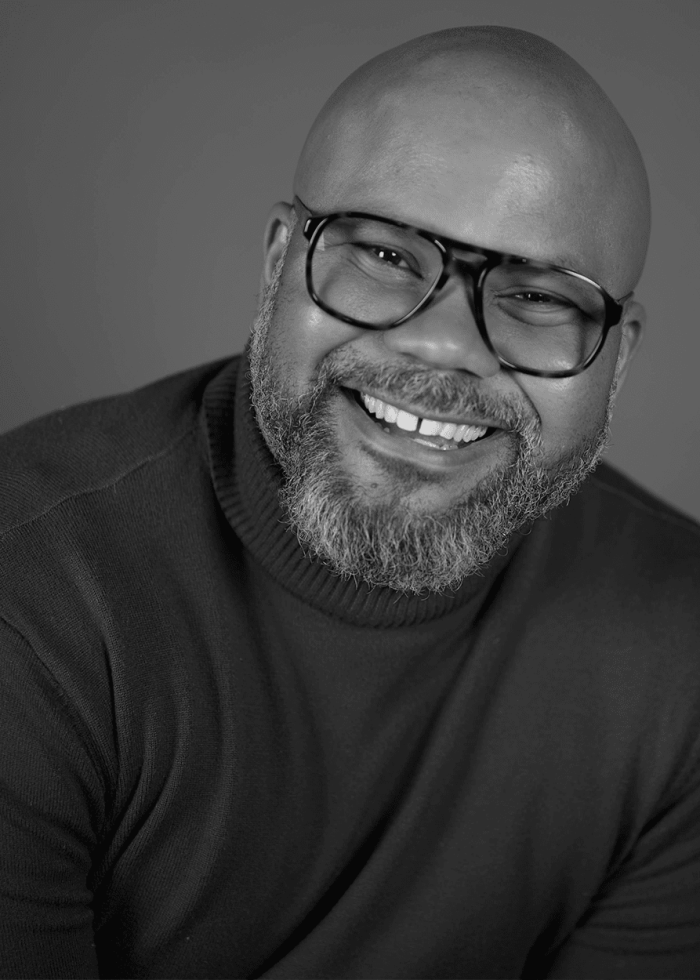 Karl O'Brian Williams smiling, wearing glasses and a turtleneck