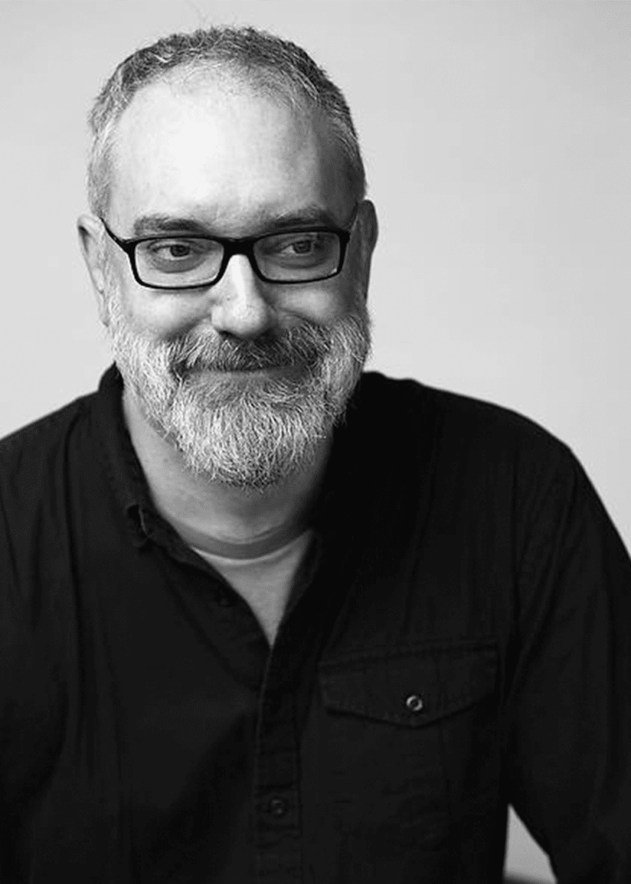 Man with gray beard and glasses smiles, looking to the side.