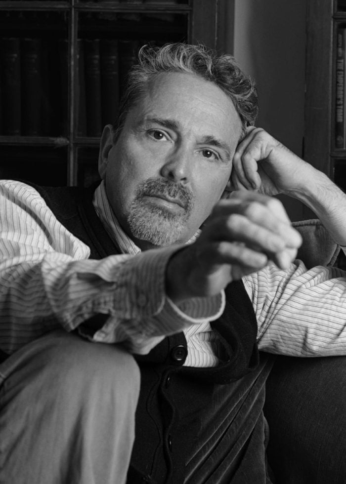 Craig Lucas, writer, poses on a couch in a library setting.
