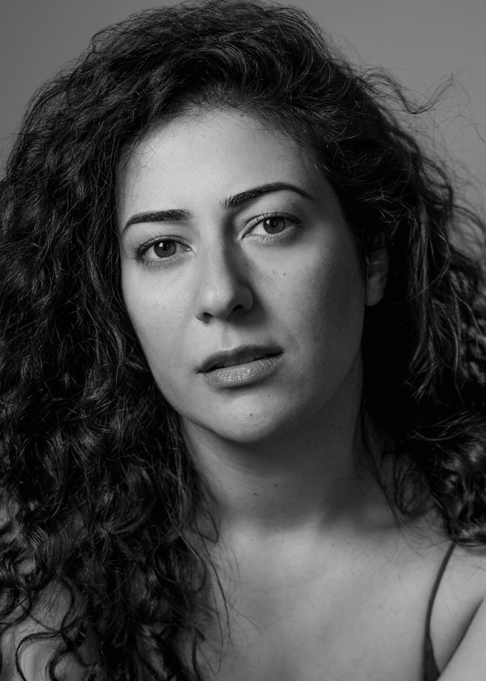 Close-up portrait of Nadine Malouf with curly hair, looking directly at the camera.