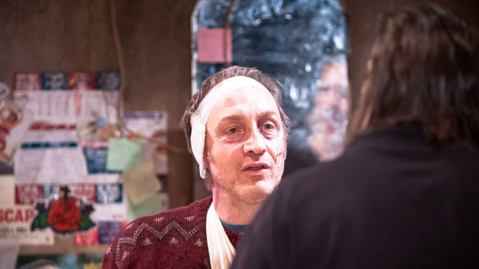 Injured man with head bandage talks to another person. The Night Alive.