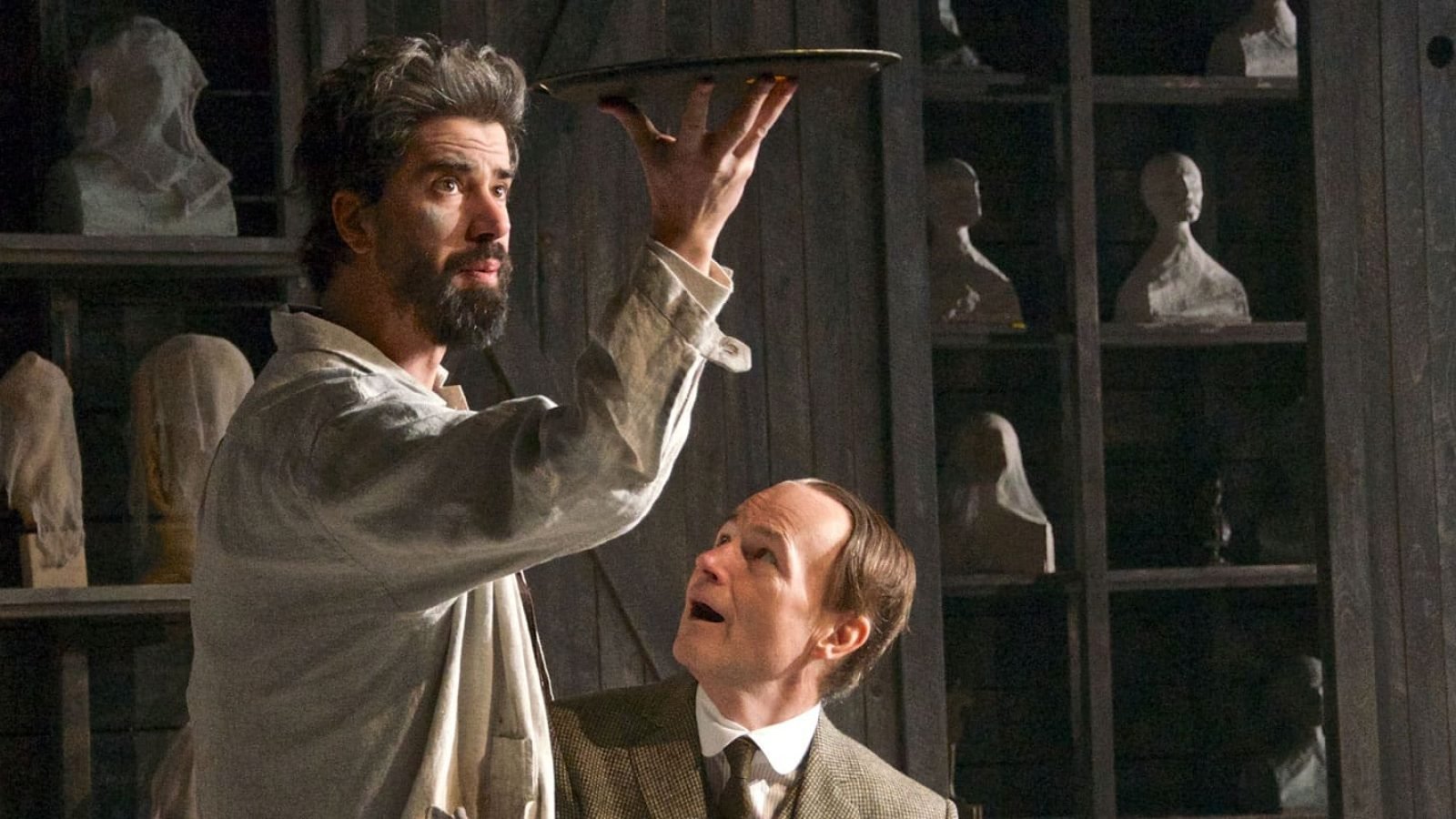 Two men in period clothing examine a plaster cast, contemplating posterity.